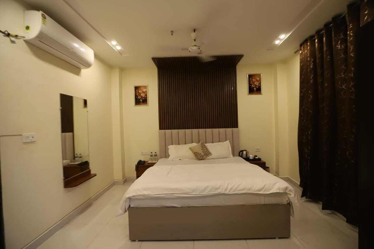 A bedroom with a large bed, a ceiling fan, an air conditioning unit, a nightstand with a lamp, and a mirror.