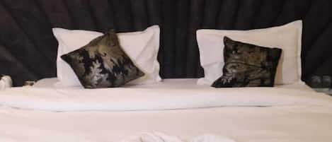 A bed with a dark headboard, white bedding, and decorative pillows.