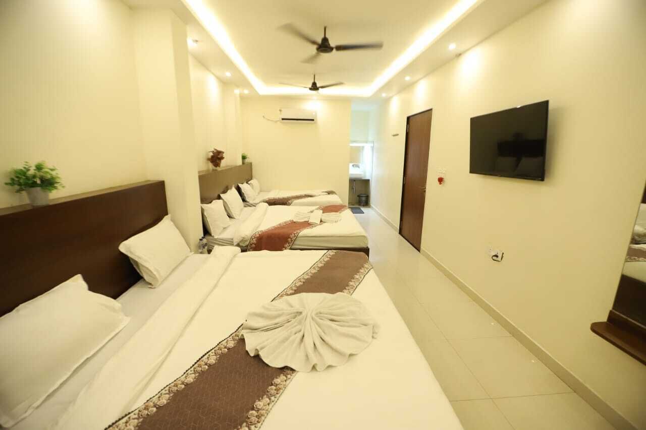 A hotel room with two beds, a ceiling fan, a TV, and a plant.