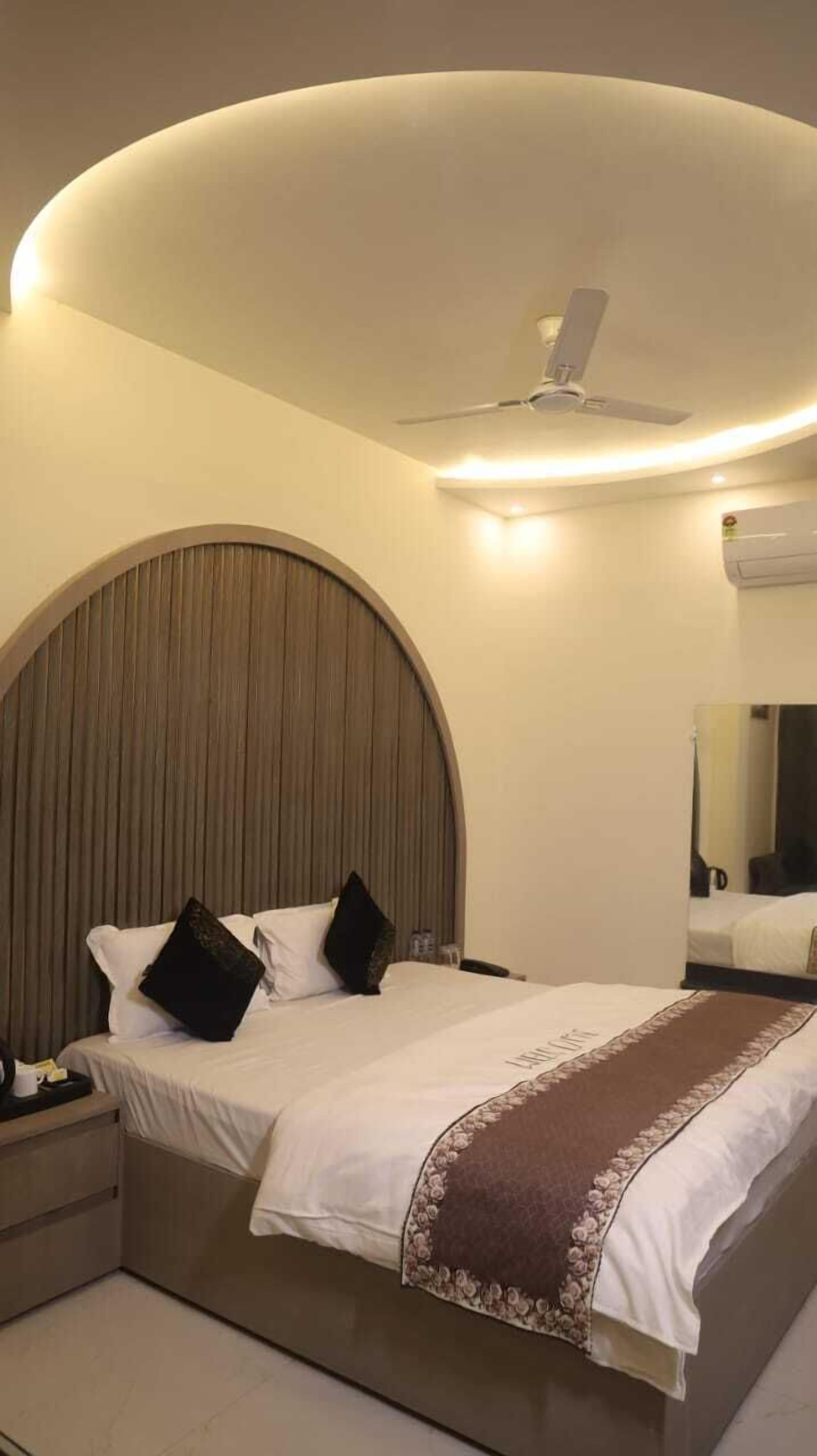 A modern hotel room with a curved ceiling, a large bed with white linens, dark pillows, and a brown decorative throw.