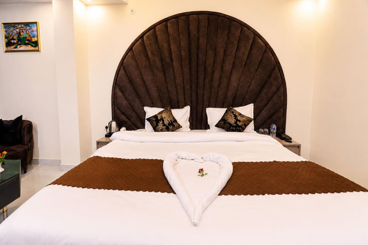 Quarto de hotel com uma cama grande, cabeceira, duas mesas de cabeceira, um criado-mudo, um quadro na parede e uma cadeira marrom.
