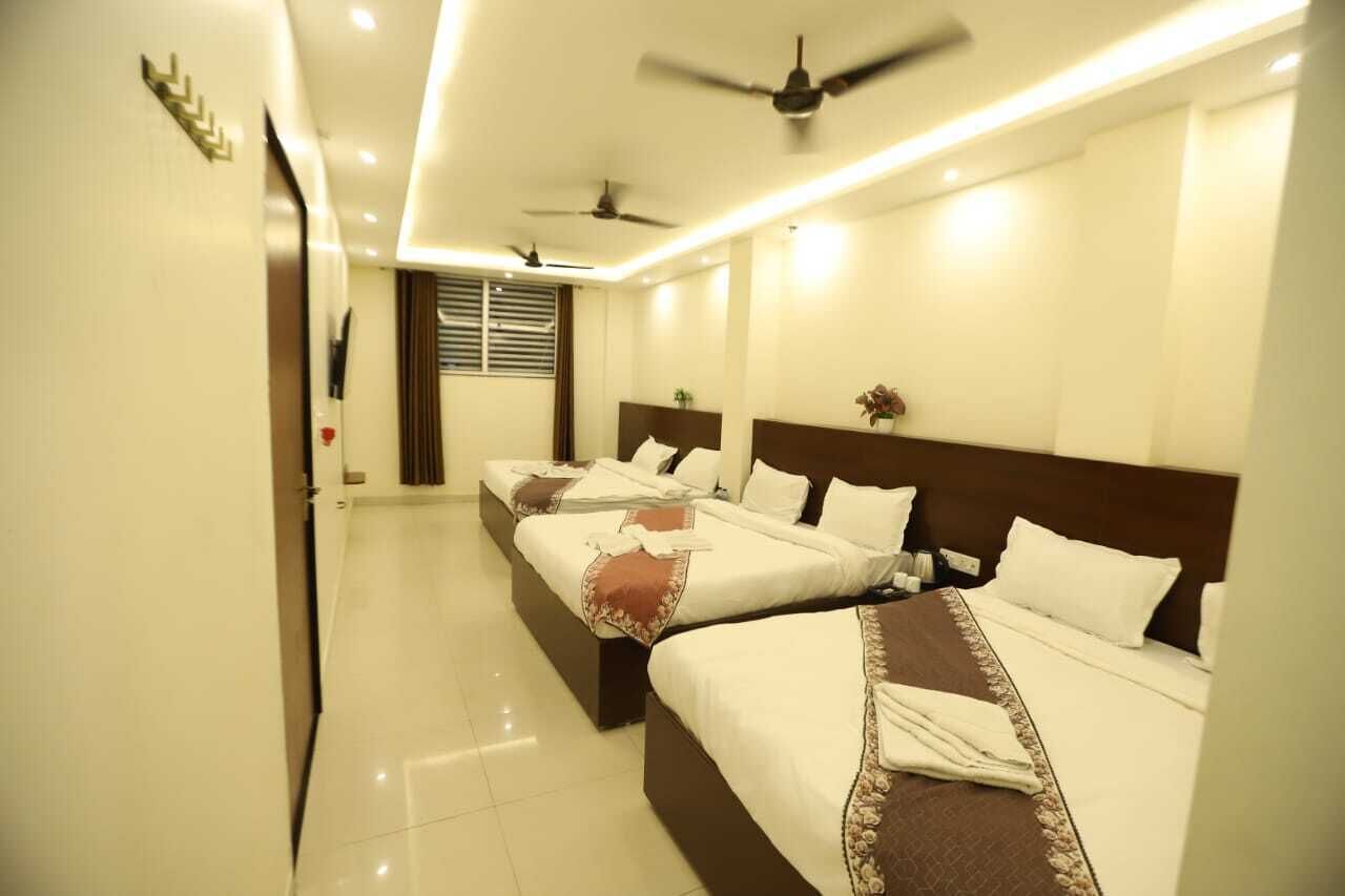 A hotel room with three beds, ceiling fans, and a large window with blinds.