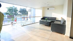 A spacious lobby with a modern black sofa, a glass partition, and a potted plant. - Hotel R Raghavam (Ayodhya)