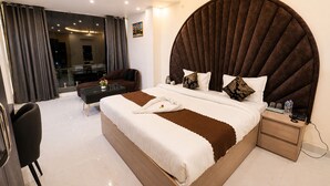 A modern hotel room with a large bed, a separate seating area, a small table, and a view of the cityscape. - Hotel R Raghavam (Ayodhya)