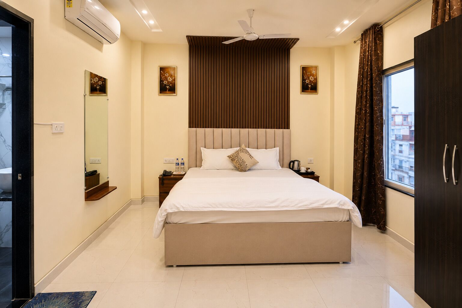 Habitación de hotel con una cama grande, ventilador de techo, ventana con cortinas y vista a la ciudad.