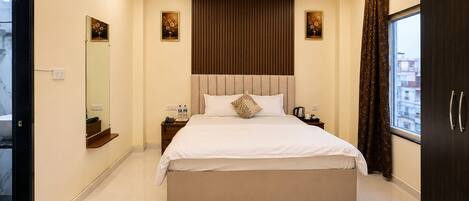 Habitación de hotel con una cama grande, ventilador de techo, ventana con cortinas y vista a la ciudad.