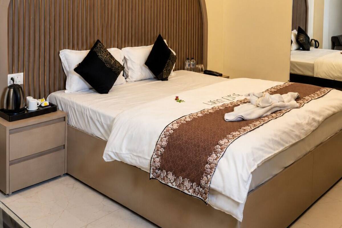 Um quarto moderno com uma cama grande, um ventilador de teto, uma mesa de cabeceira com chaleira e uma mesa de vidro.