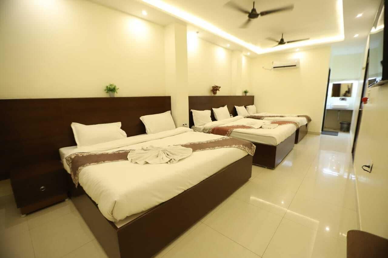Habitación de hotel con tres camas, un ventilador de techo y una planta pequeña en la pared.