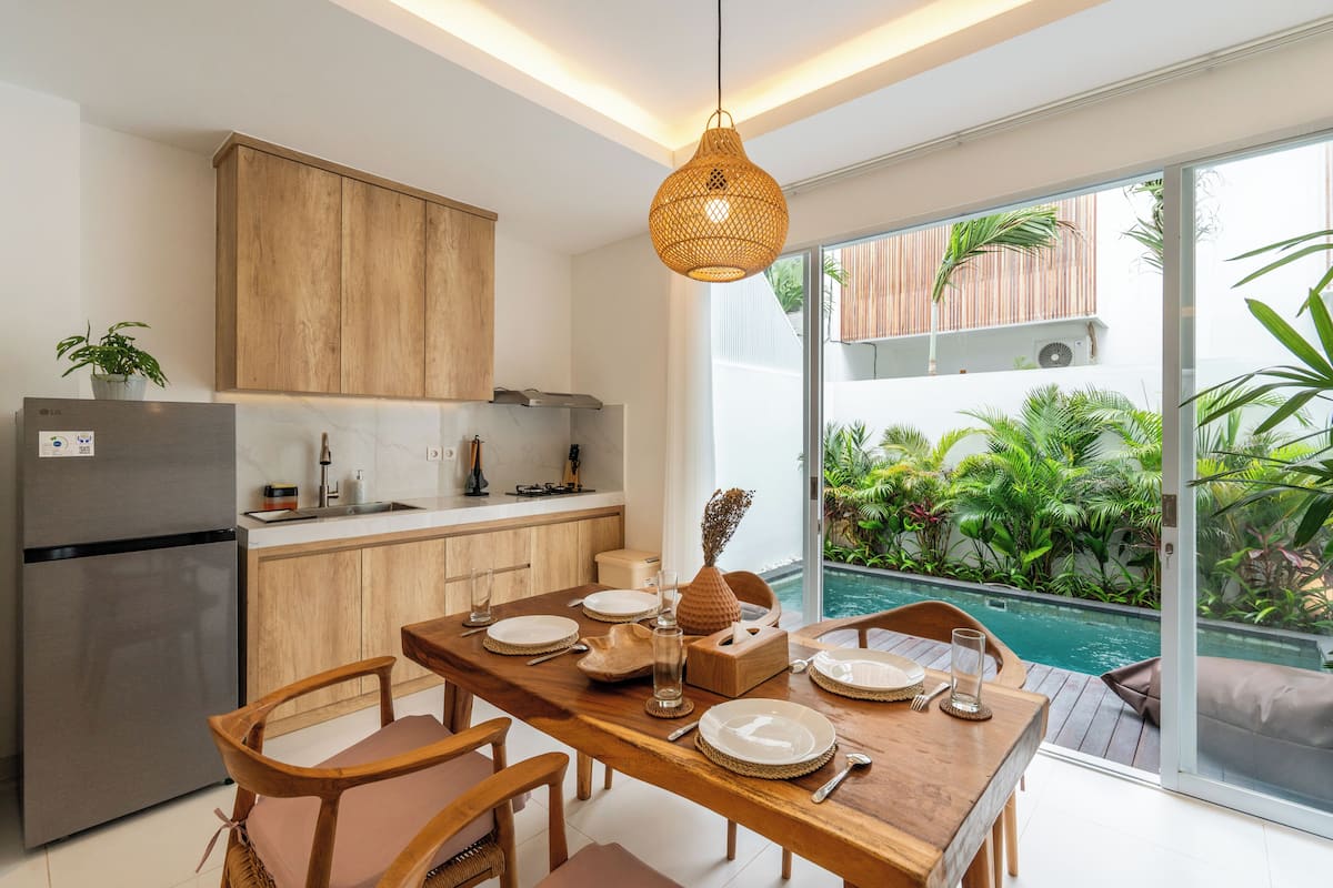 A modern kitchen with wooden cabinets, a stainless steel refrigerator, and a dining area with a wooden table and chairs.