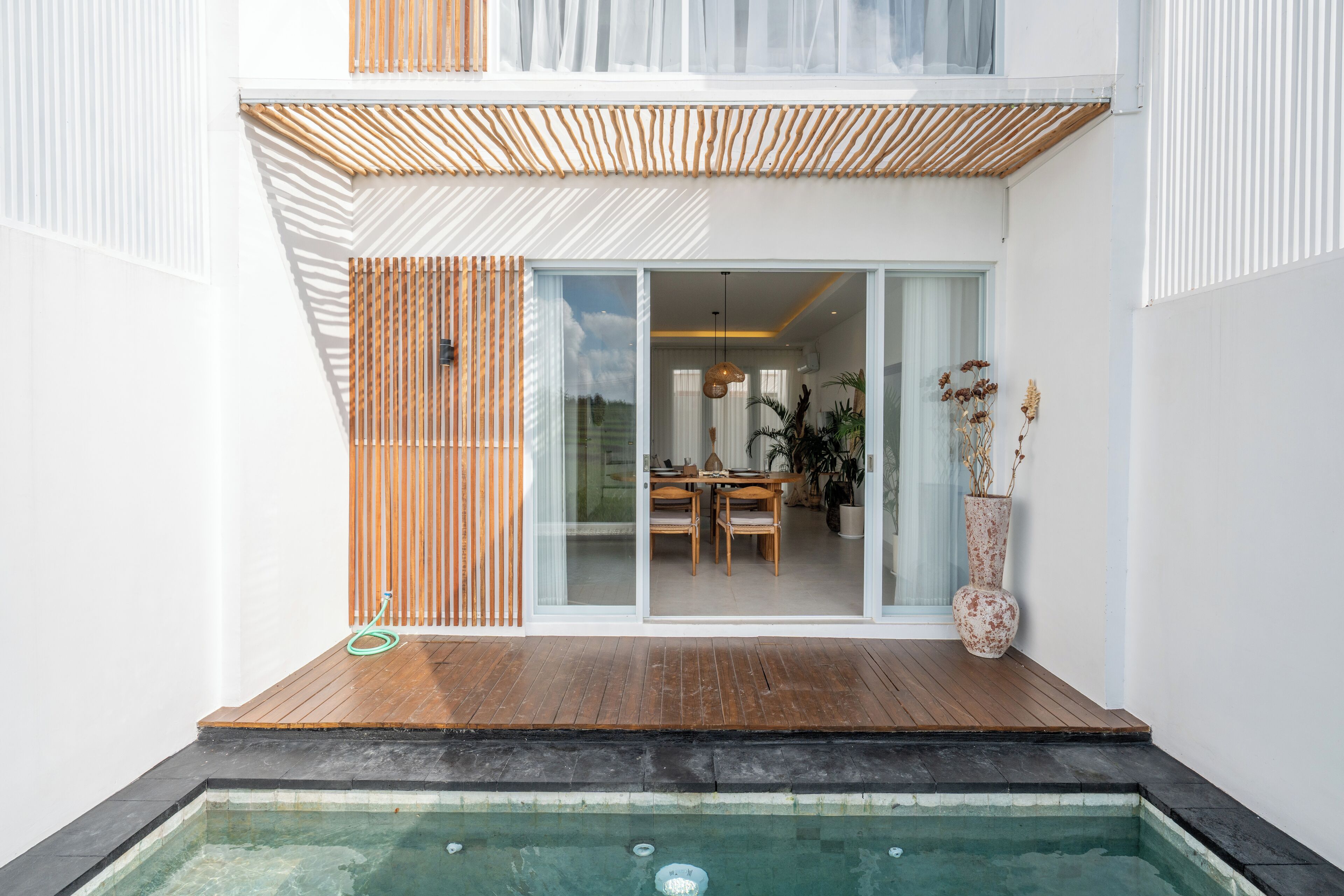 Una casa moderna con terraza de madera, puerta corrediza de vidrio que da a un comedor y una piscina pequeña.