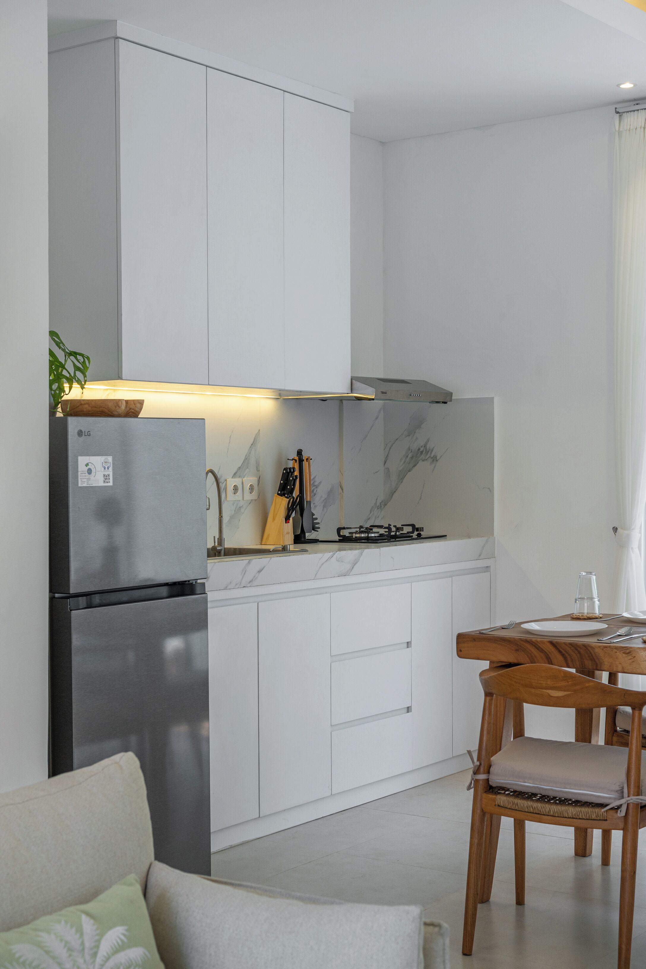 Une cuisine moderne avec des meubles blancs, un réfrigérateur en acier inoxydable, une cuisinière à gaz et une table à manger en bois avec des chaises.