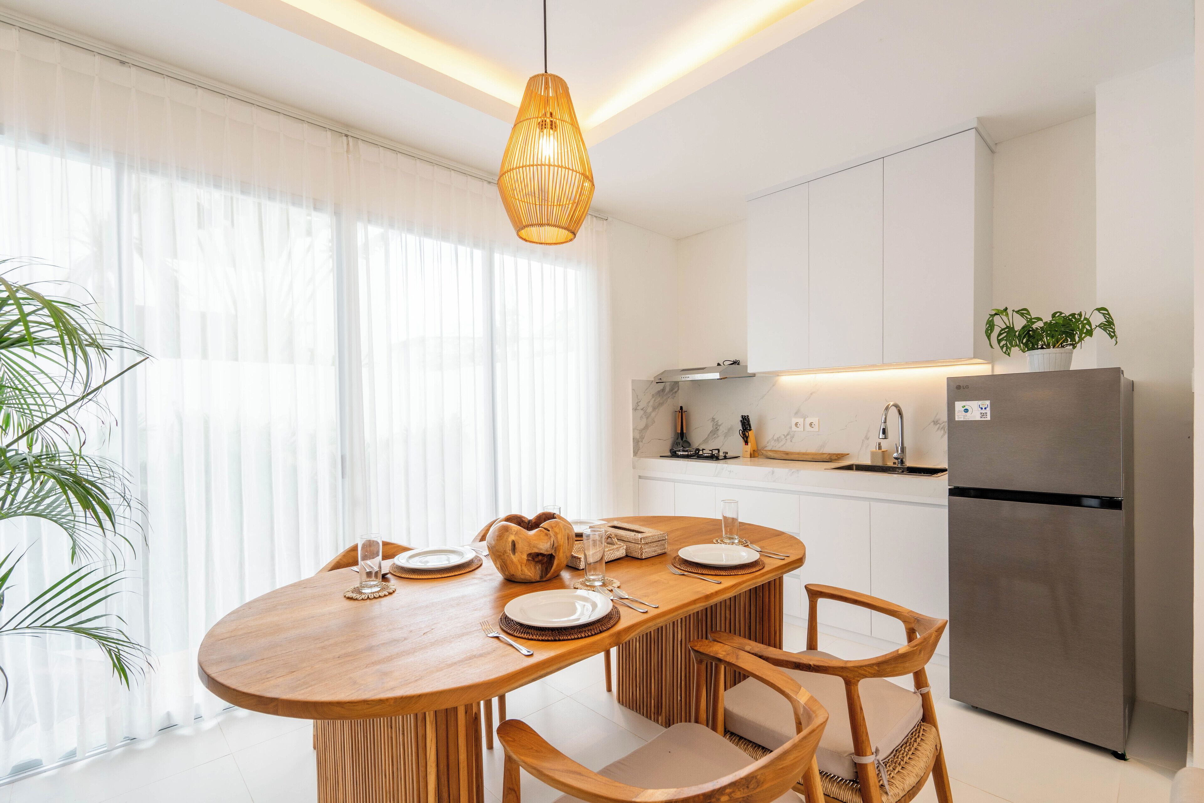 A modern kitchen with white cabinetry, a stainless steel refrigerator, and a wooden dining table set for four.