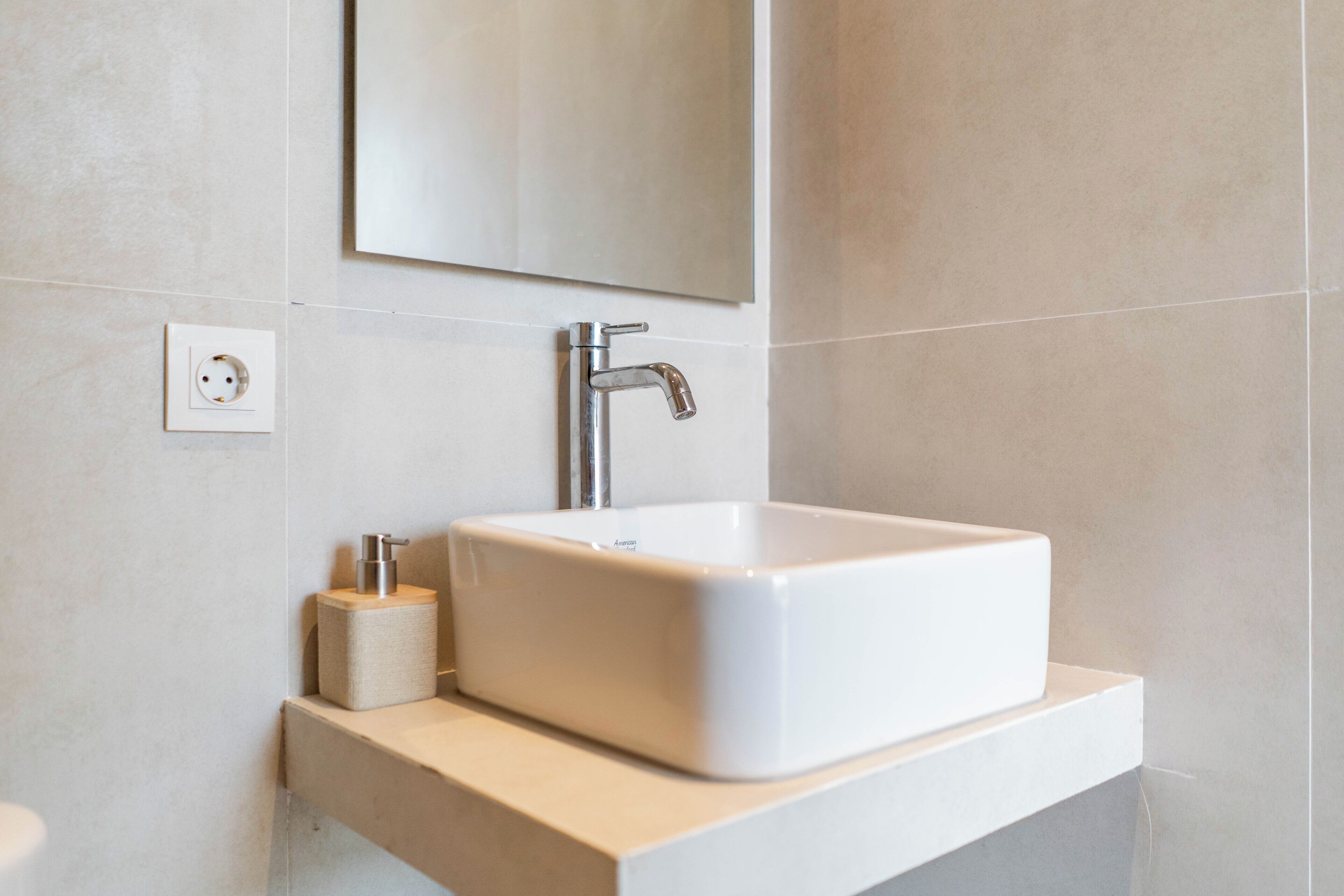 A modern bathroom with a white sink, a mirror, and a wall socket.