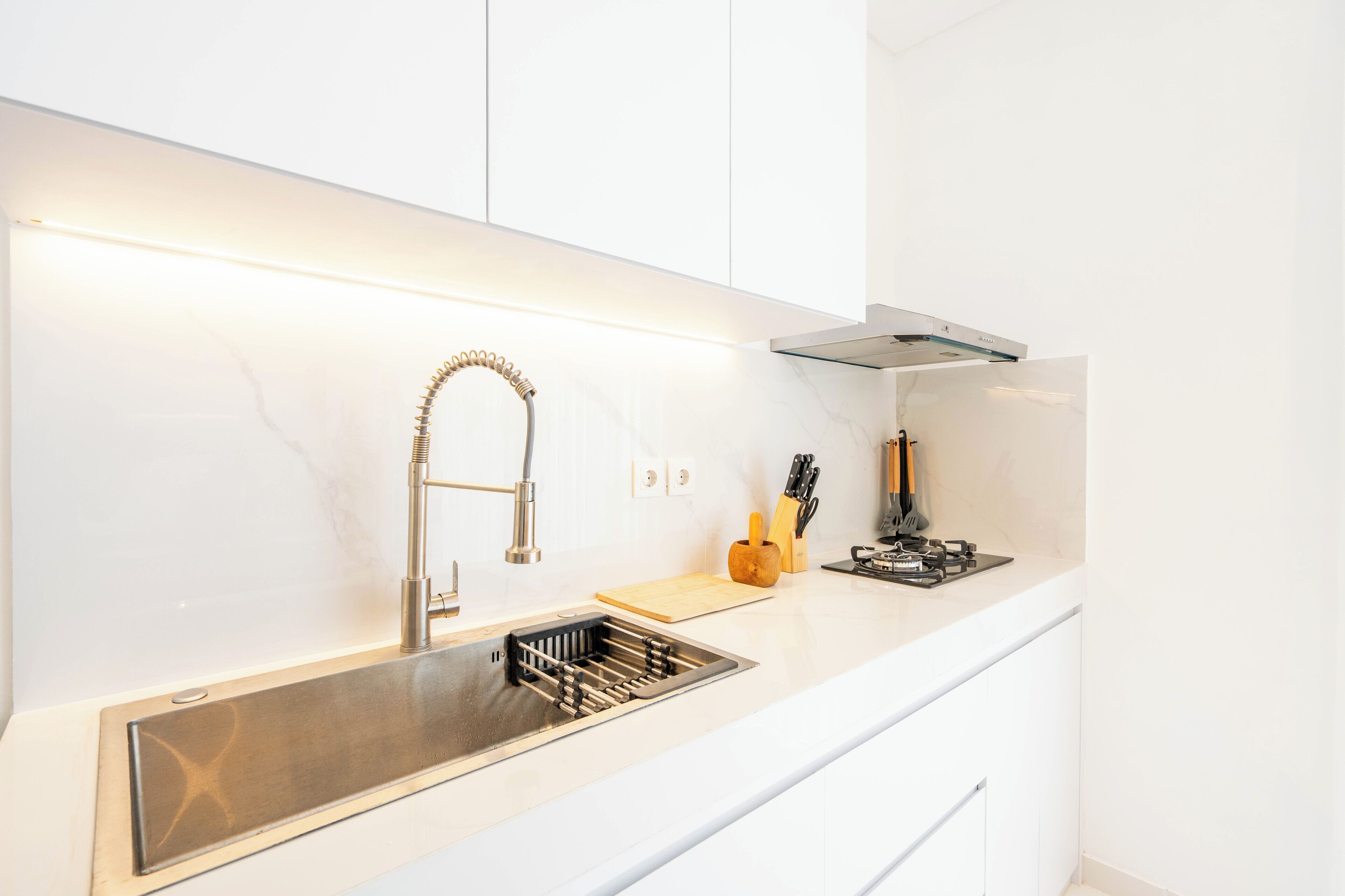 A modern kitchen with a stainless steel sink, white cabinets, and a built-in stove.
