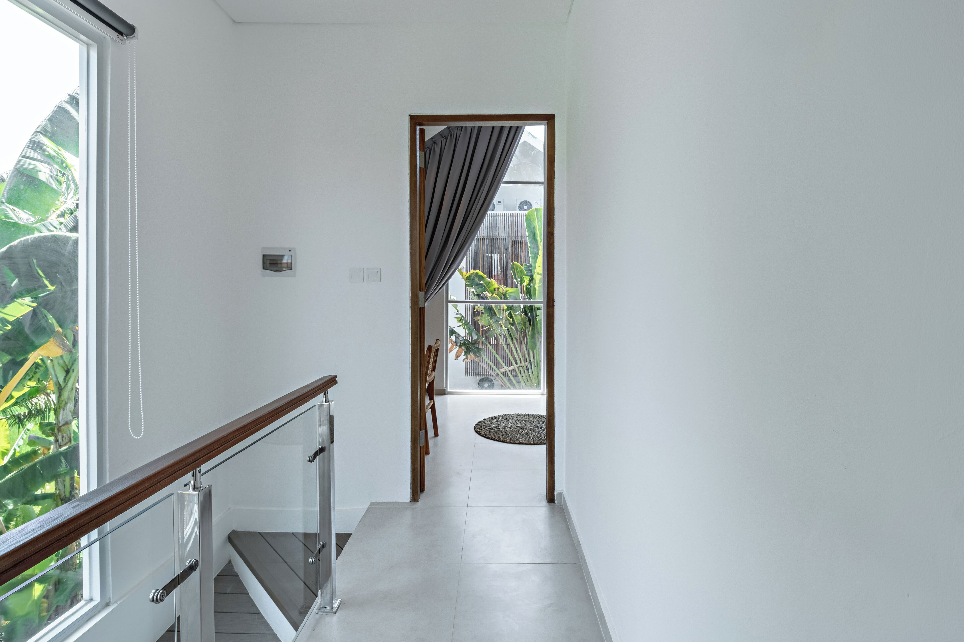 Un couloir moderne avec une rambarde en verre, une porte en bois et une vue sur un balcon agrémenté de plantes.