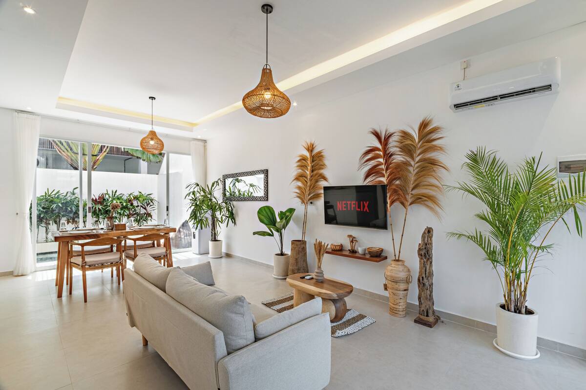 A modern living room with a sofa, dining table, chairs, and a TV mounted on the wall.