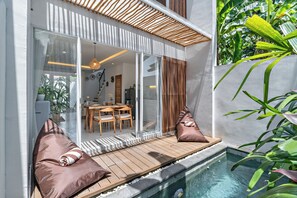 Uma área de piscina moderna ao ar livre, com deck de madeira, assentos e porta de vidro que dá para uma sala de jantar.