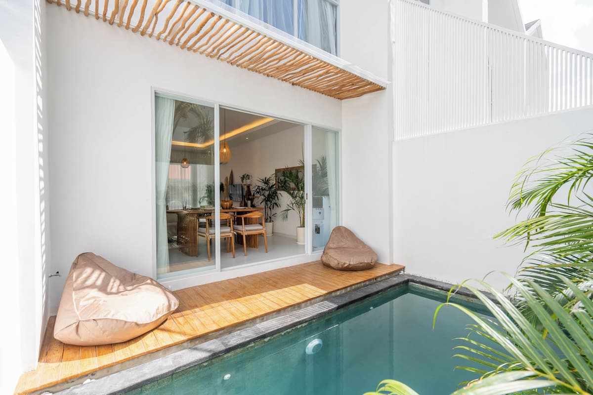 A modern poolside area with a wooden deck, a glass door leading to an interior space, and two bean bags.