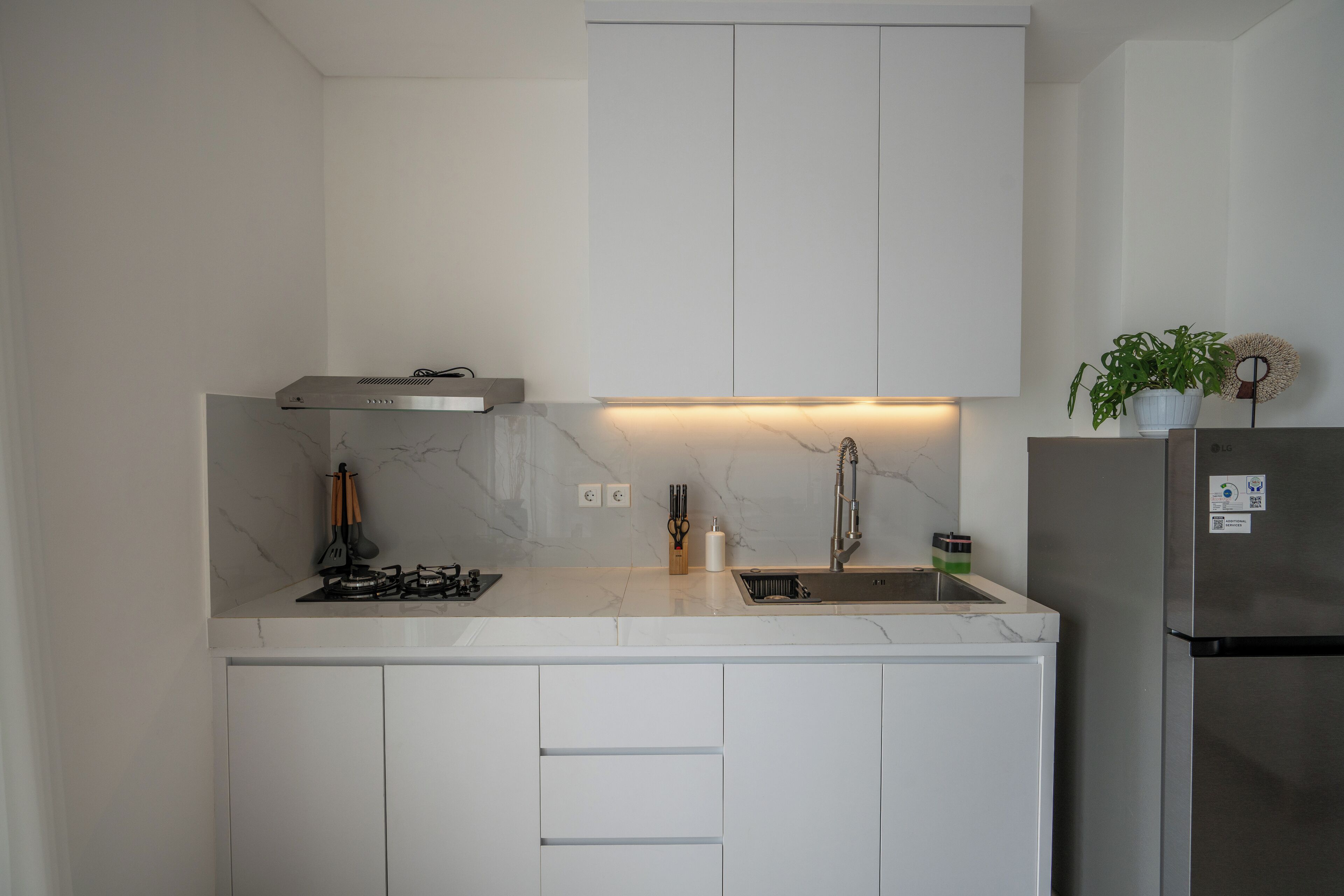 A modern kitchen with white cabinets, a stainless steel refrigerator, and a marble countertop.