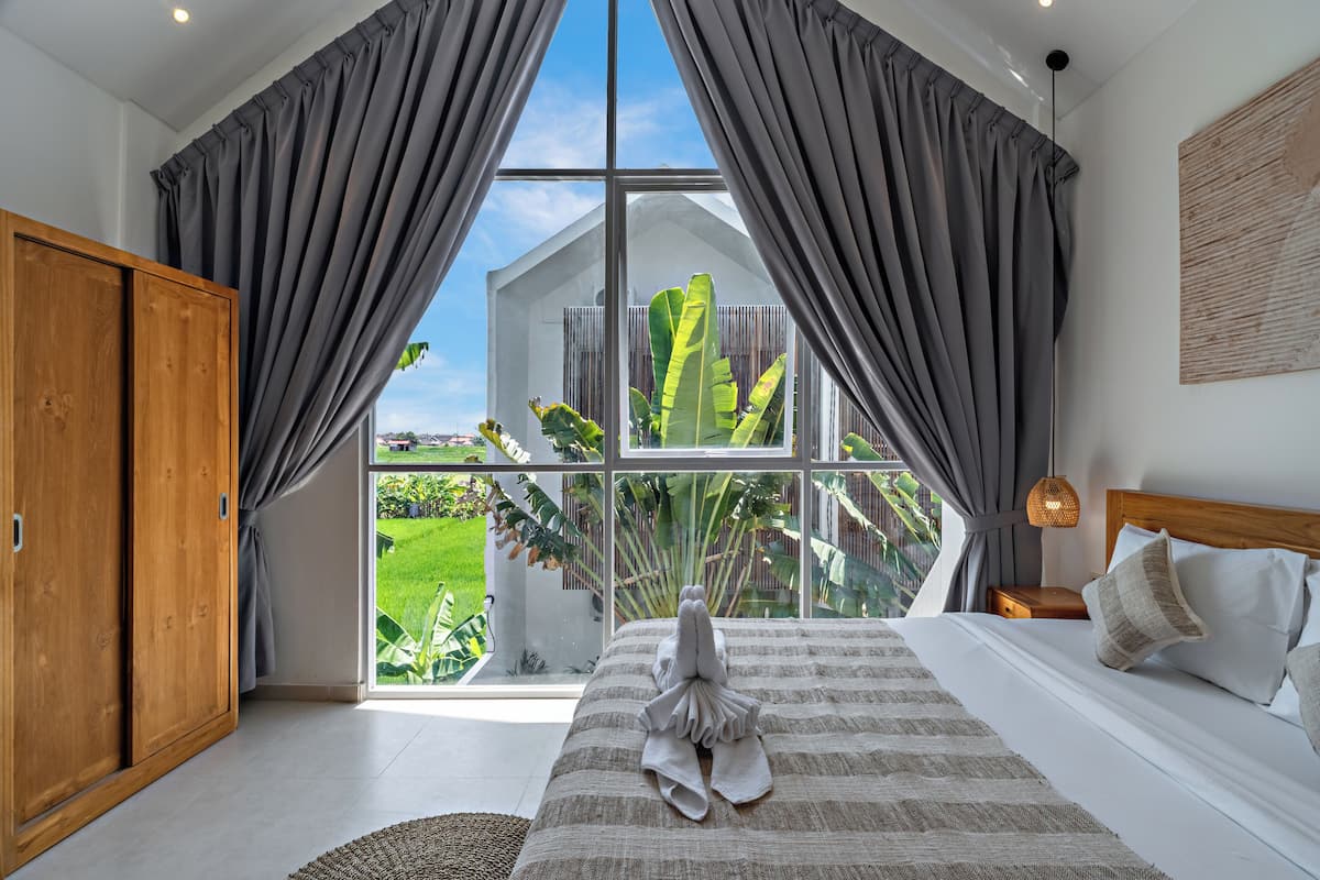 A bedroom with a large window, a bed with a towel, and a view of greenery outside.