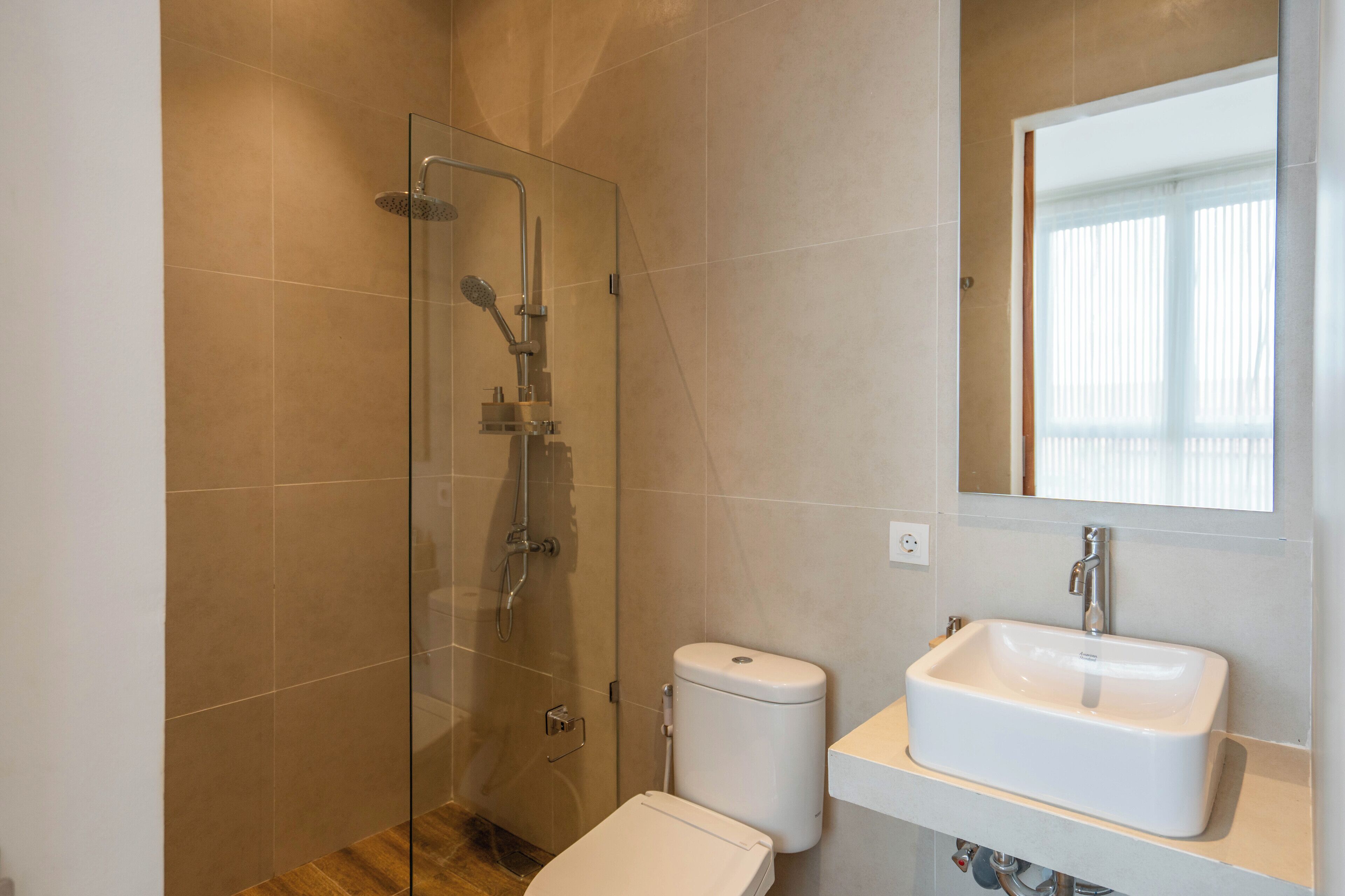 Un baño moderno con ducha envuelta en vidrio, inodoro blanco y lavamanos con espejo sobre él.