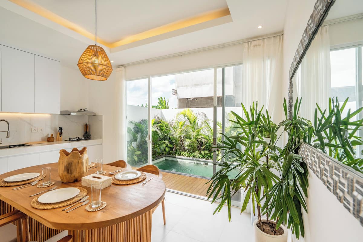 A modern kitchen with a dining area, large windows, and a view of a swimming pool.