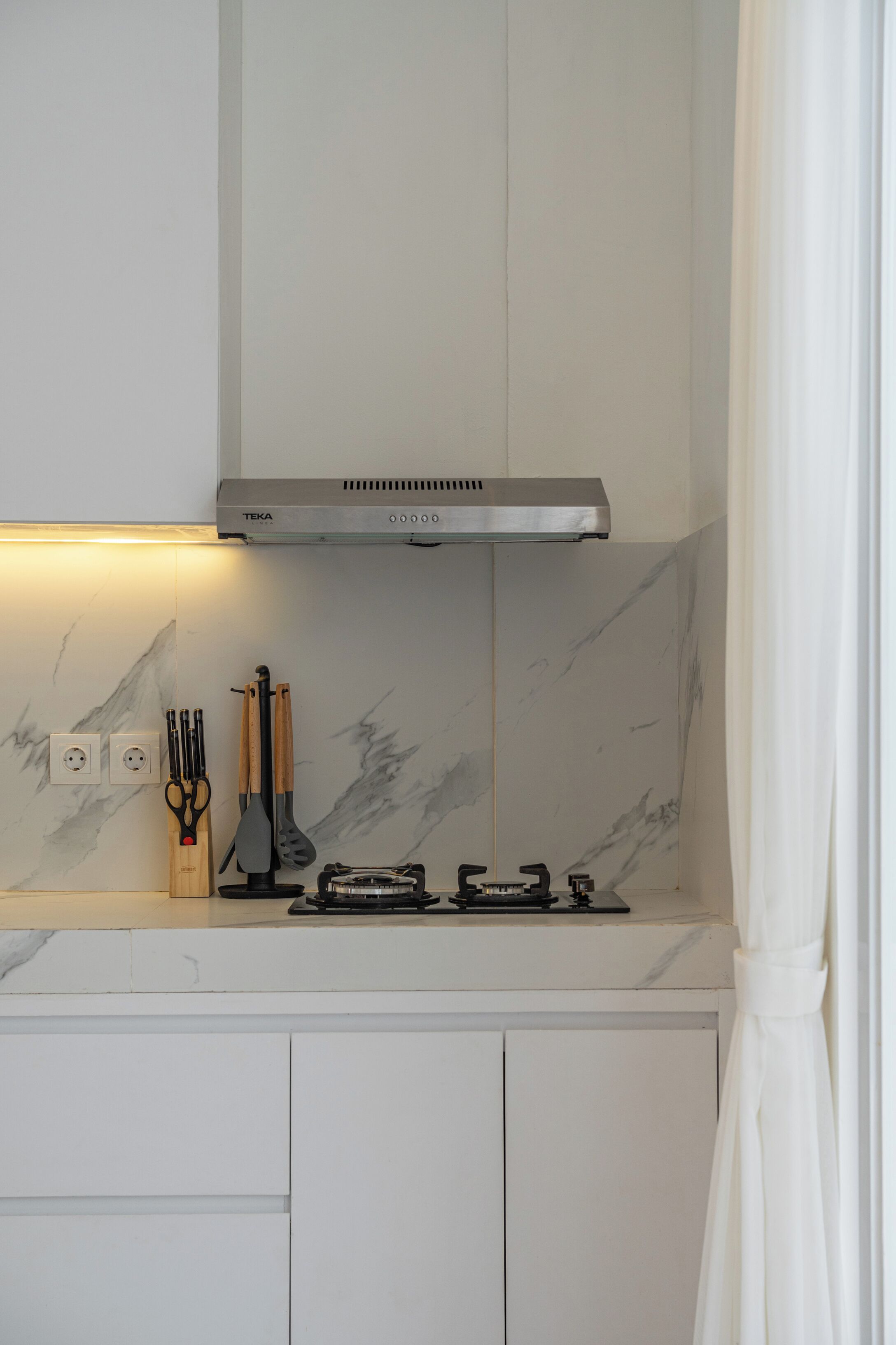 A kitchen with a stainless steel range hood, marble backsplash, and white cabinetry.
