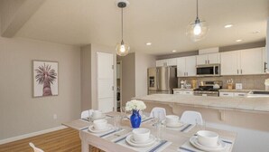 A modern kitchen with white cabinets, a central island, and a dining area with a wooden table set for four.