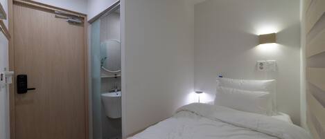 Un dormitorio con puerta de madera, un baño con inodoro y lavamanos, y una lámpara de noche.