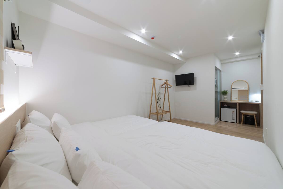 Un dormitorio con cama, escritorio, silla, televisor y un mueble pequeño.