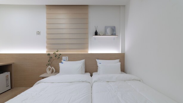 Een moderne hotelkamer met twee bedden, een houten hoofdbord, een klein plankje met decoratieve items en een nachtkastje met een vaas.