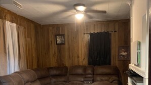 A living room with a sectional sofa, wooden walls, a ceiling fan, and a fireplace. - Luverne St, Magnolia MN RoomB Beautiful place to visit (Magnolia)