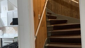 A wooden staircase with a handrail, leading to a room with white walls and a kitchen area visible in the background. - Luverne St, Magnolia MN RoomB Beautiful place to visit (Magnolia)