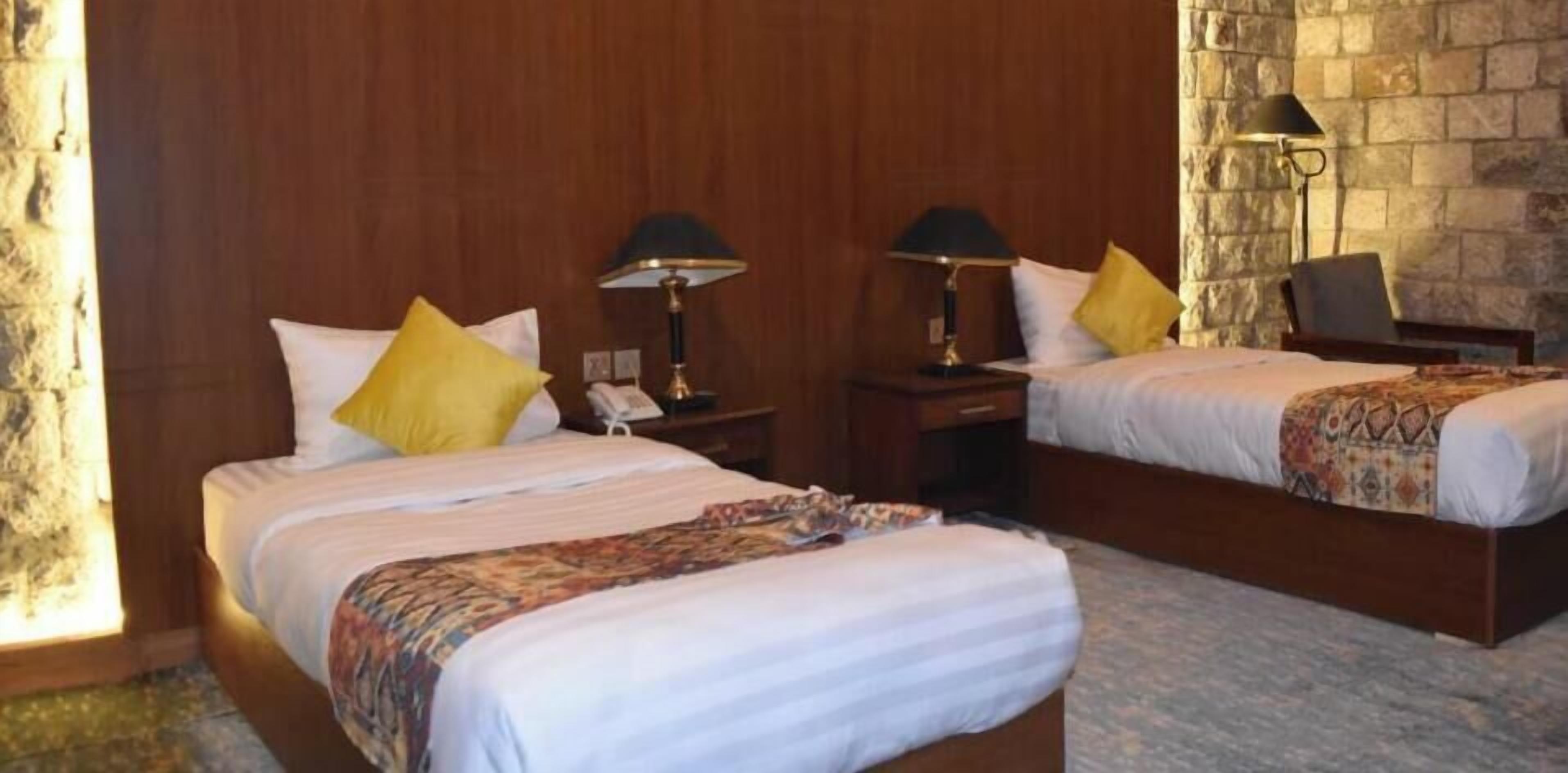 Een hotelkamer met twee bedden, houten hoofdborden, een stenen muur en een lamp op elk nachtkastje.