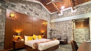 A bedroom with a wooden ceiling, stone walls, a bed with yellow pillows, a desk, and a chair. - Destination Hotel Khaplu (Khaplu)