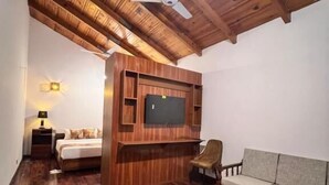 A room with a wooden ceiling, a ceiling fan, a flat-screen TV mounted on a wooden panel, a sofa, a chair, and a wooden coffee table. - Destination Hotel Khaplu (Khaplu)