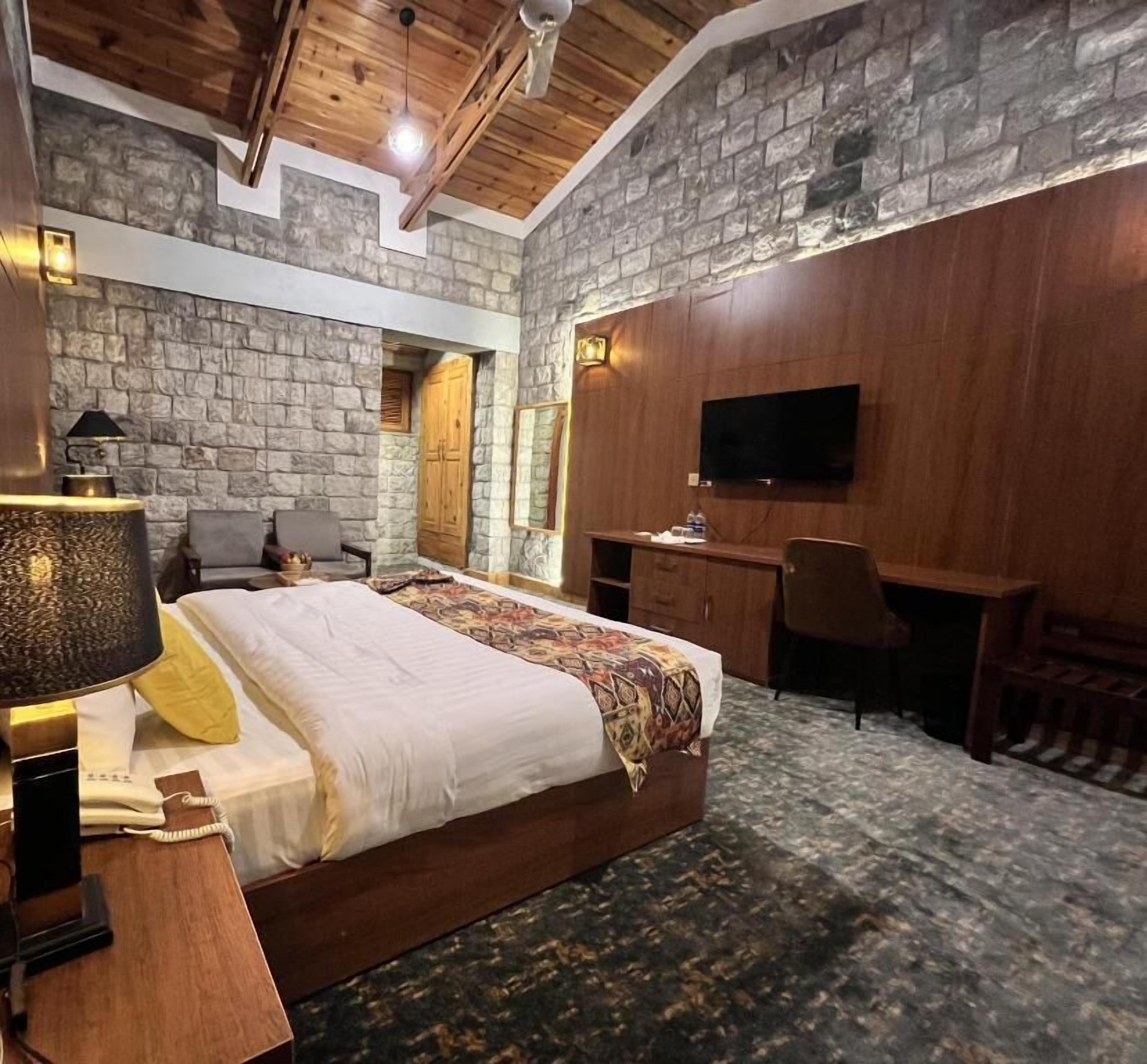 A bedroom with a bed, desk, chair, and TV.