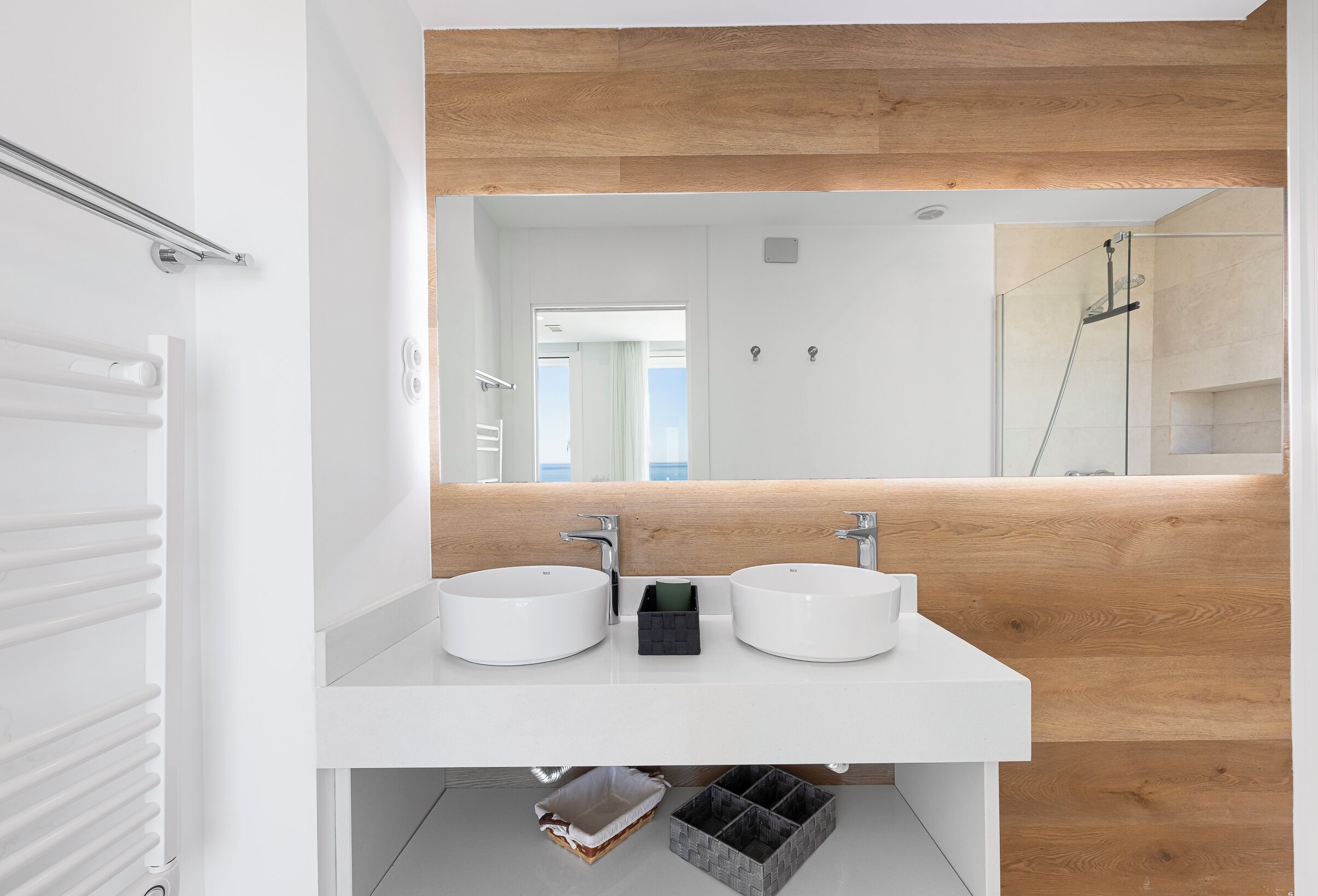 Een moderne badkamer met twee witte wastafels, een houten accentmuur en een grote spiegel.