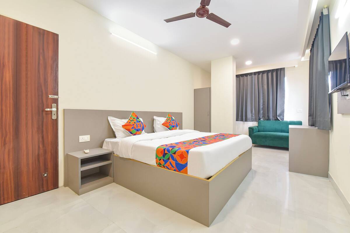 A modern hotel room with a large bed, a desk, a green sofa, and a ceiling fan.