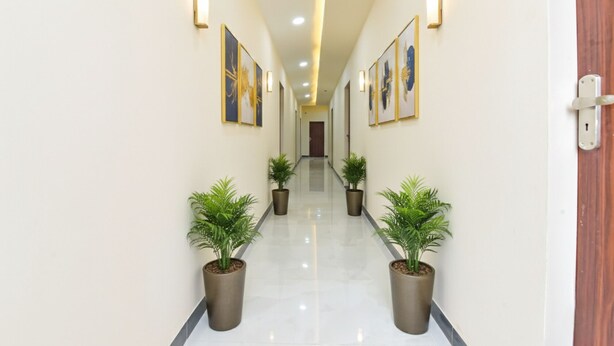A hallway with potted plants, framed artwork on the walls, and recessed lighting. - Fabhotel Cozzy Stay (Jaipur)
