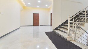 A spacious hallway with a wooden door, a staircase with metal railings, and a modern ceiling with recessed lighting. - Fabhotel Cozzy Stay (Jaipur)