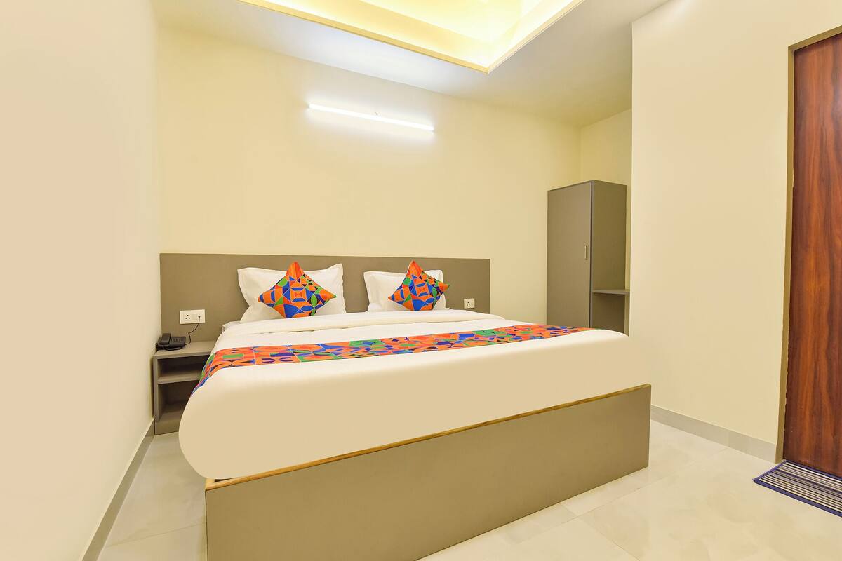 A modern hotel room with a large bed, a bedside table, a nightstand, a wardrobe, and a door.