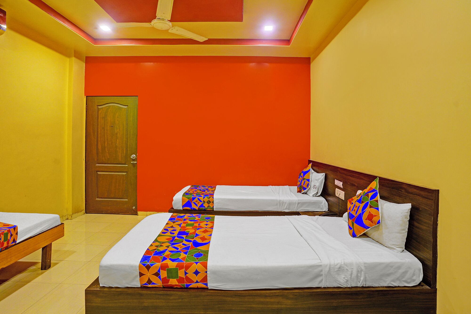A hotel room with two beds, a wooden door, and a ceiling fan.