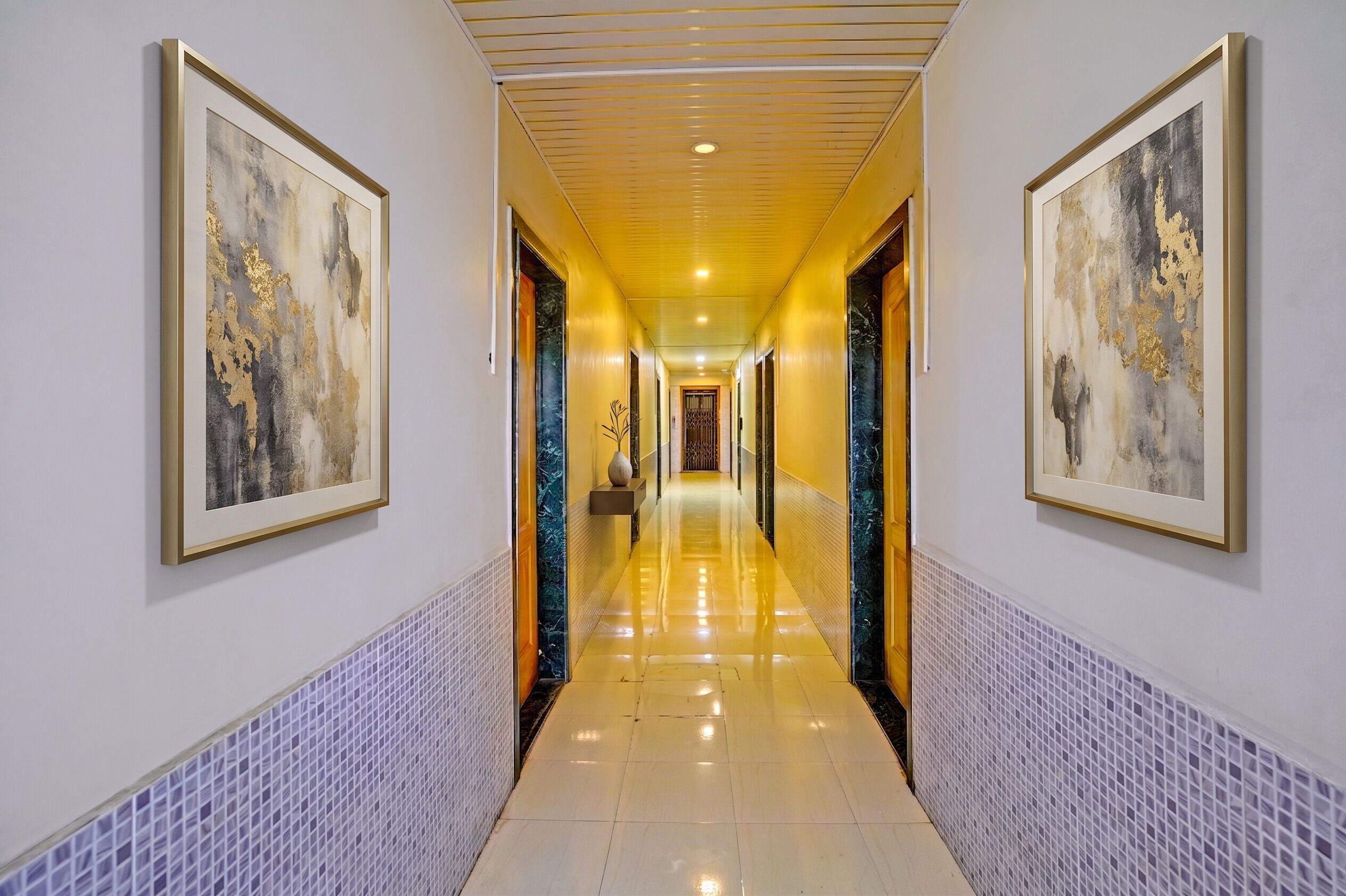 A hallway with framed abstract art, a tiled floor, and a central door leading to another room.