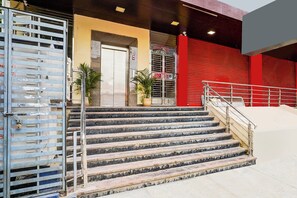 A set of outdoor stairs leading to a building entrance with a metal gate and a red wall. - FabHotel Golden Stay - JP nagar Metro (Bengaluru)