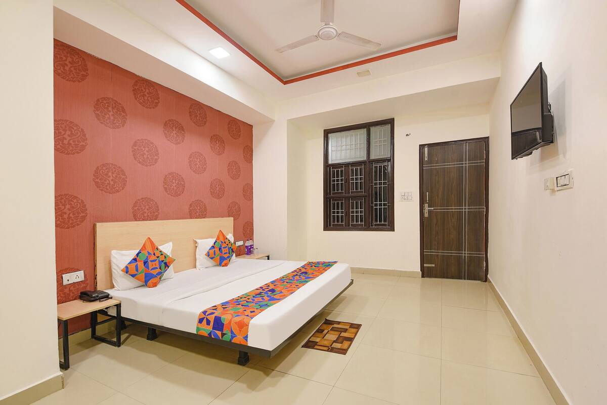 A hotel room with a bed, a nightstand, a TV mounted on the wall, and a window with bars.