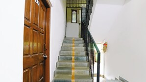 A staircase with a wooden door on the left and a fire extinguisher on the right. - Fabhotel Peaceful Studio Aai Bungalow (Panvel)