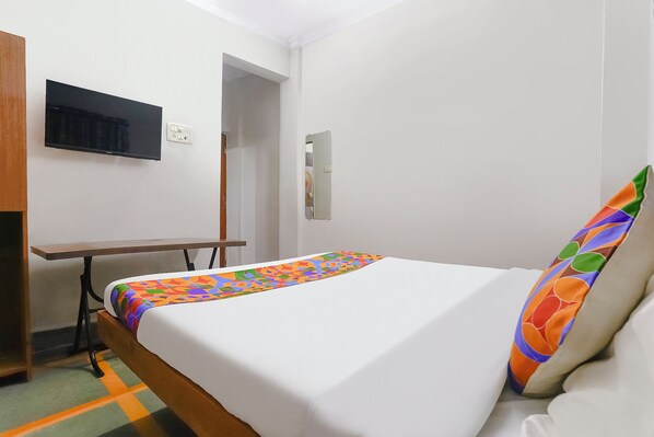 A hotel room with a bed, a desk, a TV, and a mirror.