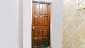 A wooden door with a metal handle and a keyhole, set in a hallway with white walls and patterned tiles. - Fabhotel Peaceful Studio Aai Bungalow (Panvel)