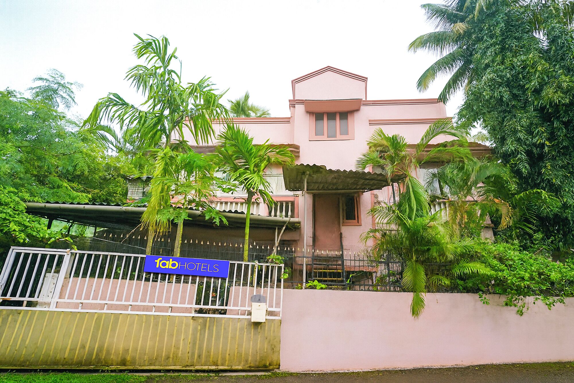 A pink building with a gated entrance, surrounded by lush greenery and palm trees.